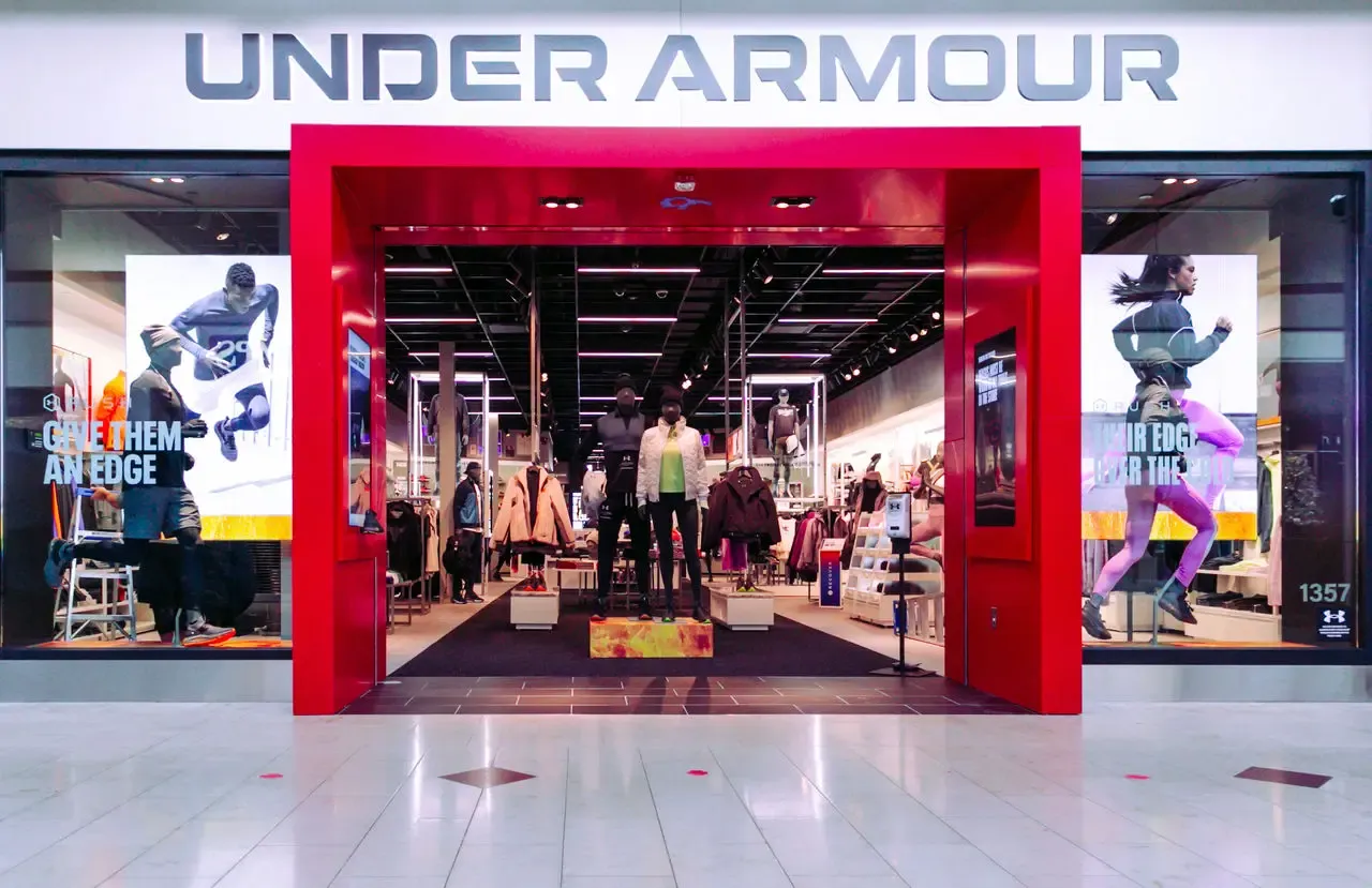Under Armour store with a red-framed entrance, mannequins in sportwear, and large athletic posters on each side. (image: Under Armour)