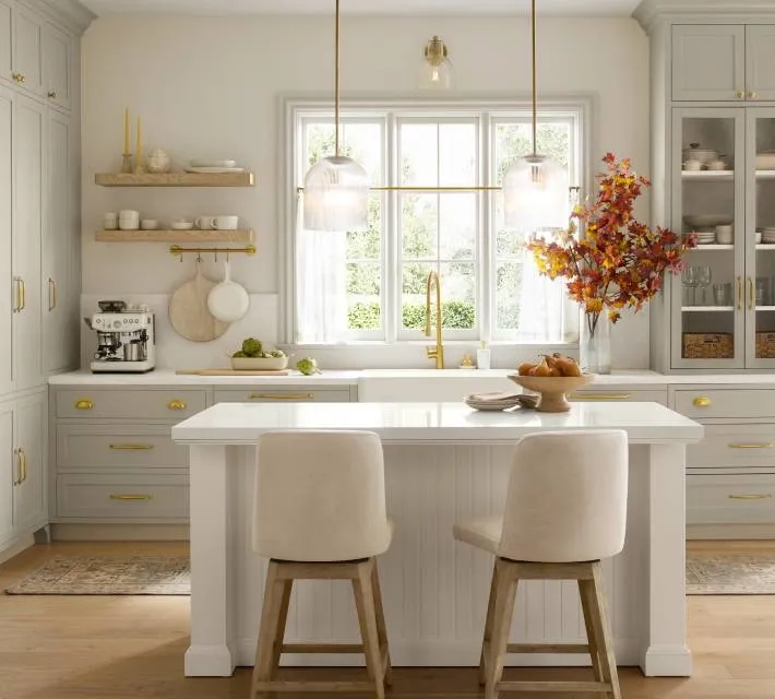 A bright, elegant kitchen with light gray cabinets, a white island, and warm gold accents, styled with cozy modern decor.