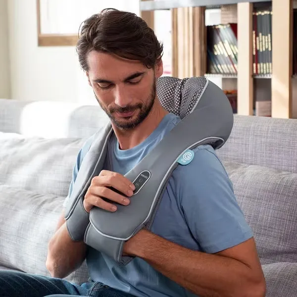 A man is using a neck and shoulder massager while sitting on a sofa.