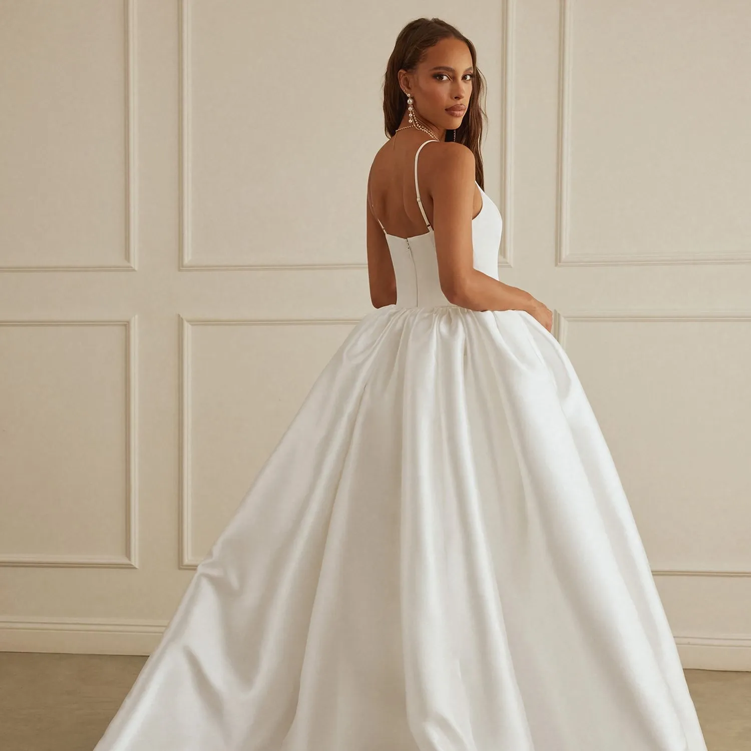 A woman wearing a white, elegant wedding dress poses gracefully in a minimalist room.