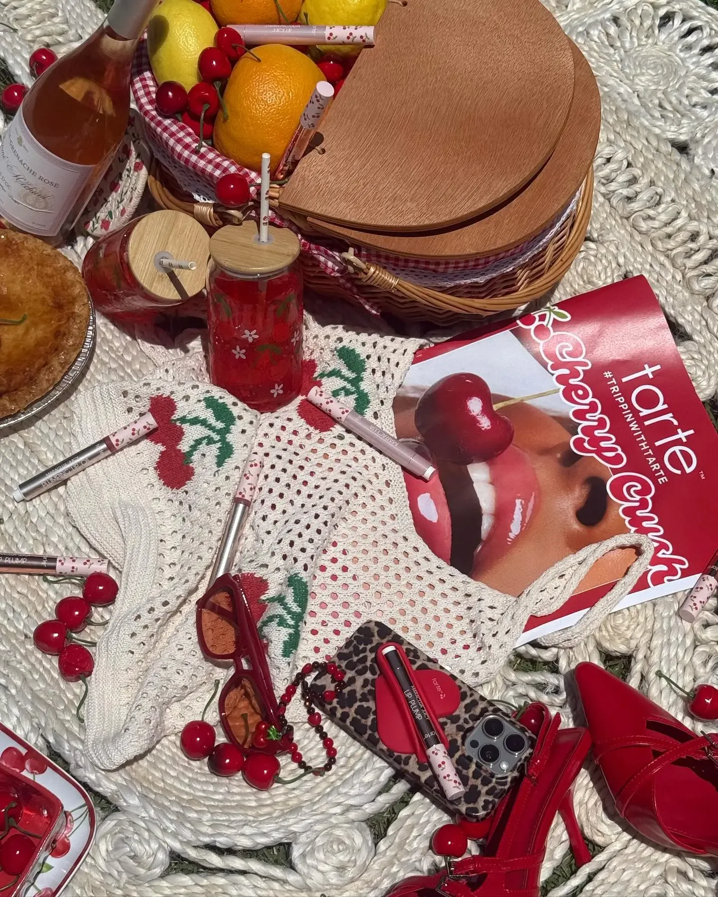 A vibrant picnic setup with cherries, fruity drinks, Tarte makeup, and chic red accessories.