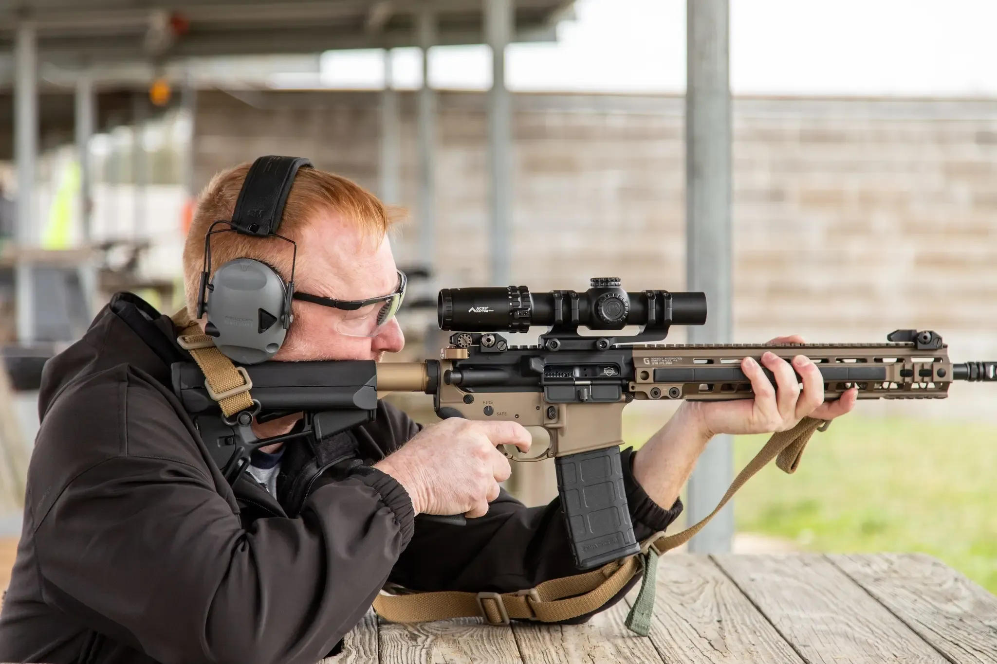 A man at a shooting range aims a scoped rifle.