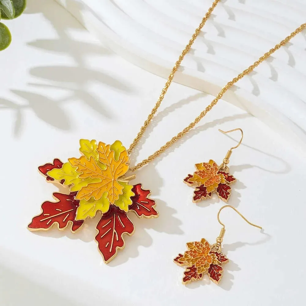A gold necklace and earrings feature colorful autumn leaf designs.