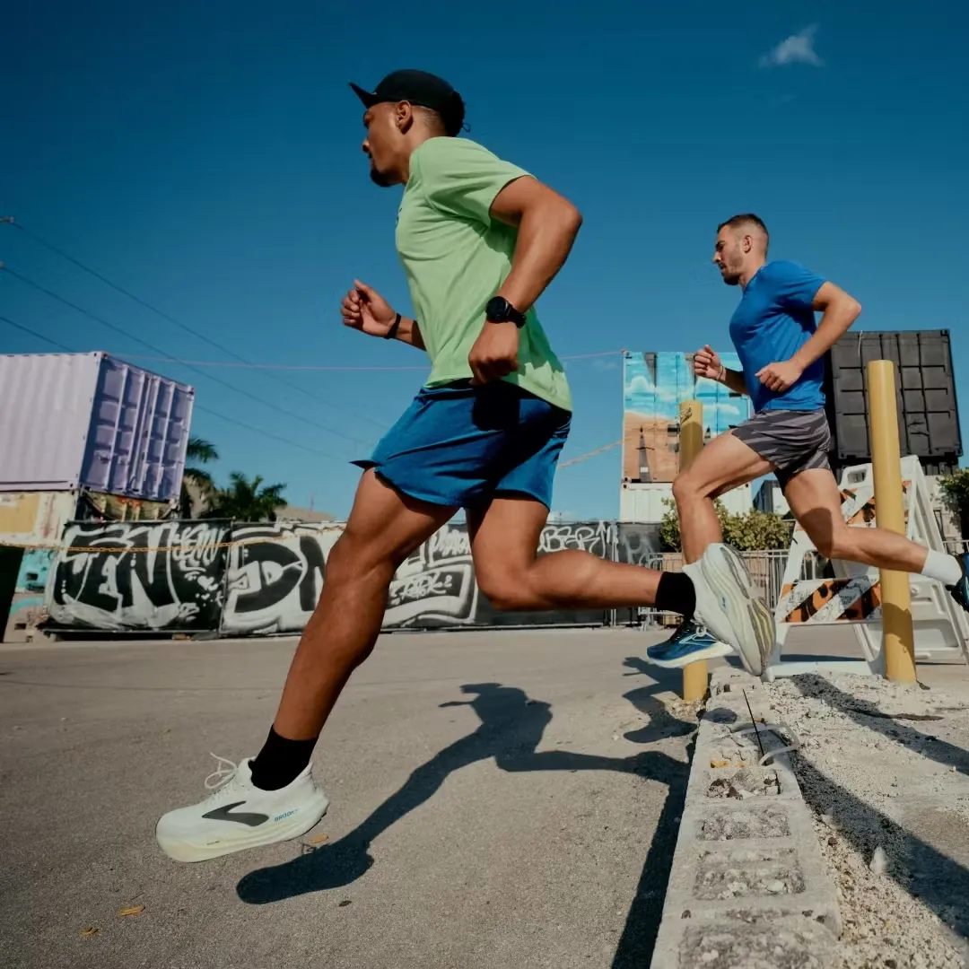 Two men running outdoors in athletic gear under a clear blue sky.
