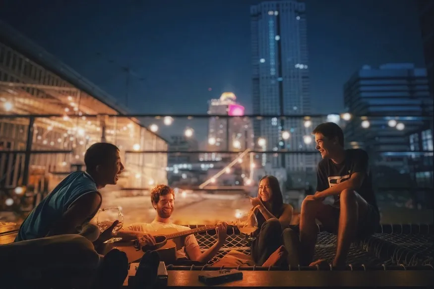 Friends hanging out on a rooftop at night with music and city lights.