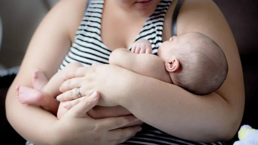 Parent holding baby monitor receiver while checking on sleeping infant in nursery bedroom