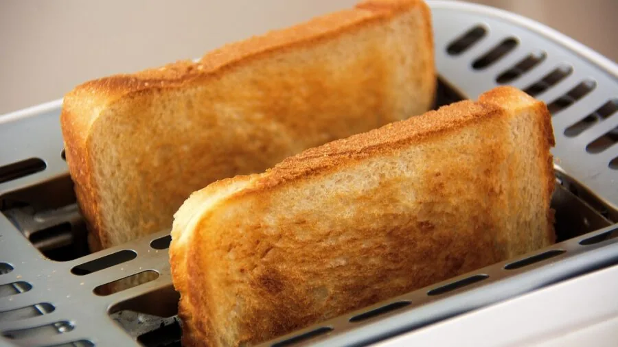 Person enjoying fresh golden toast at breakfast table with morning light streaming through window