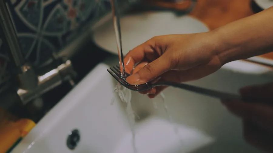 Person washing dishes in modern kitchen sink with natural light