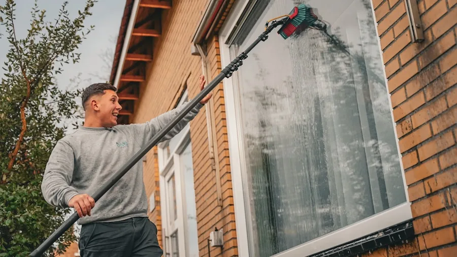 Person washing home exterior with water spray during residential cleaning maintenance